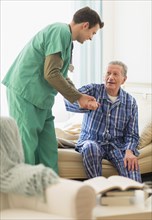 Caucasian nurse helping patient out of bed in home