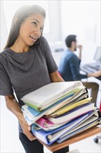 Hispanic businesswoman carrying stack of folders in office