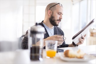 Hispanic man reading newspaper at breakfast