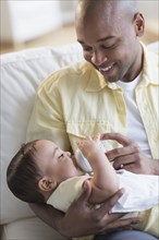 Smiling father feeding baby on sofa