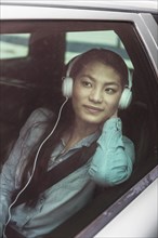 Mixed race teenage girl listening to headphones in backseat of car