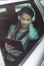 Mixed race teenage girl using digital tablet in backseat of car