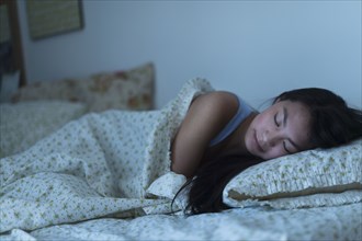 Mixed race teenage girl sleeping in bed