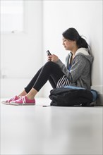 Mixed race teenage girl using cell phone in school hallway
