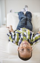 Mixed race boy laying upside-down on armchair