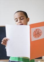 Mixed race boy reading report on basketball in class
