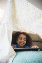 African American girl using tablet computer in blanket fort