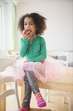 African American girl eating apple at kitchen table