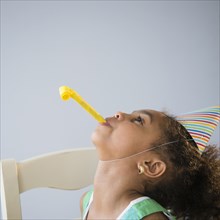 African American girl blowing noisemaker at birthday party