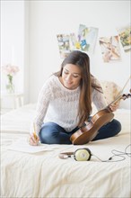Woman playing violin and taking notes on bed