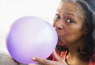 Mixed race woman blowing balloon on sofa