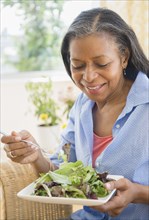 Mixed race woman eating salad on sofa