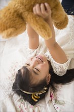 Filipino girl playing with teddy bear on bed