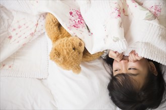 Filipino girl playing with teddy bear in bed