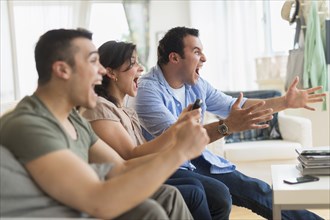 Hispanic friends cheering at television in living room