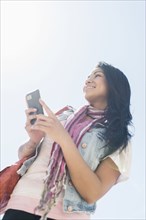 Mixed race woman using cell phone under blue sky