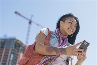 Mixed race woman using cell phone under blue sky