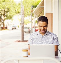African American man using laptop at sidewalk cafe