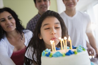 Hispanic girl blowing out candles on birthday cake