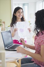 Hispanic girl proudly showing drawing to mother