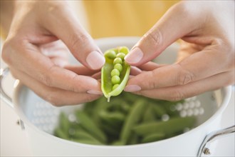 Close up of mixed race man shucking peas into colander