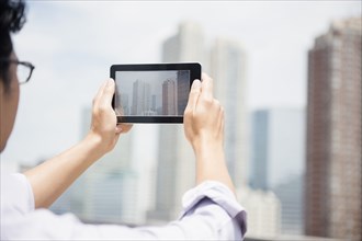 Close up of mixed race man photographing city skyline with digital tablet