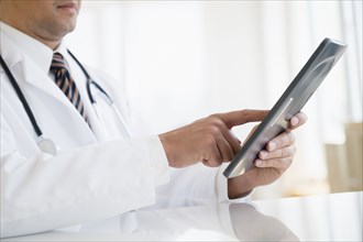 Close up of mixed race doctor using digital tablet