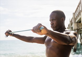 Mixed race man using resistance band on beach