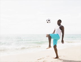 Mixed race man playing with soccer ball on beach