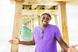 Mixed race man smiling under pier on beach