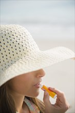 Caucasian woman applying sunscreen lip balm at beach
