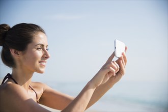 Caucasian woman taking selfie with cell phone at beach