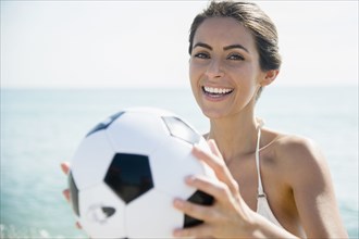 Caucasian woman holding soccer ball on beach