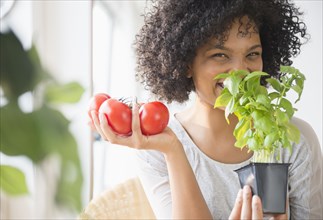 Smiling woman with tomatoes smelling plant