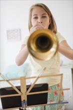 Caucasian girl practicing trumpet with digital tablet