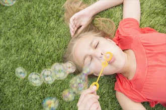 Caucasian girl blowing bubbles on grassy lawn