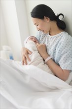 Asian mother holding newborn baby in hospital bed