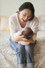 Asian mother holding baby on bed