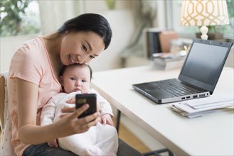 Asian mother and baby taking selfie in home office