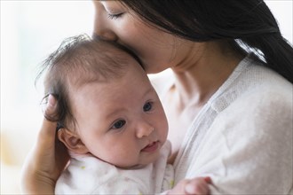 Asian mother holding and kissing baby