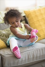 Mixed race girl pulling on socks in living room