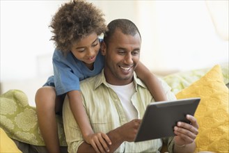 Father and son using digital tablet together in living room