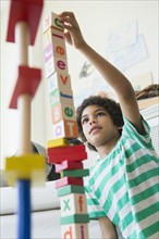 Mixed race boy building wooden block tower in living room