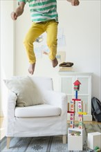 Mixed race boy jumping on armchair in living room