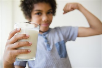 Mixed race boy flexing his muscle and drinking glass of milk