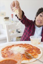 Mixed race boy sprinkling cheese on homemade pizza