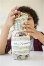 Mixed race boy putting allowance in savings jar
