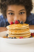 Mixed race boy admiring plate of pancakes and berries