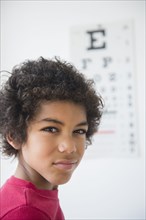 Mixed race boy squinting near eye chart