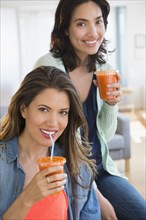 Hispanic women drinking healthy carrot juice in living room